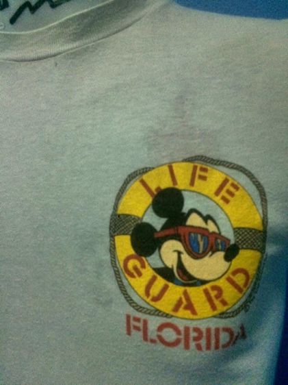 เสื้อยืดมิกกี้เมาส์ ด้านหน้าสกรีนหน้ามิกกี้อยู่ในห่วงยาง LIFE GUARD FLORIDA ด้านหลังสกรีนมิกกี้ยืนถือร่ม The Walt Disney Company ผ้า 50 50 รูปที่ 3