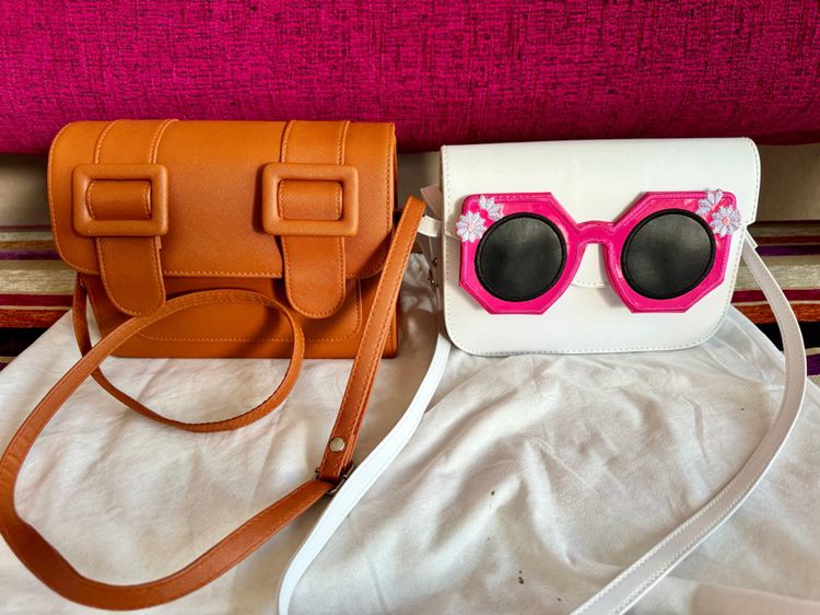 กระเป๋าสะพาย Merimies ของแท้สภาพดีมาก ใช้งานน้อย  มีสองใบ สีน้ำตาลและสีขาวมีแว่นตาสีชมพูติดอยู่ด้านหน้า 